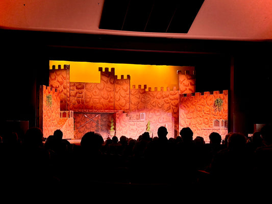 A vibrant theatrical stage set for Once Upon a Mattress, featuring castle-themed scenery illuminated in warm, golden tones.