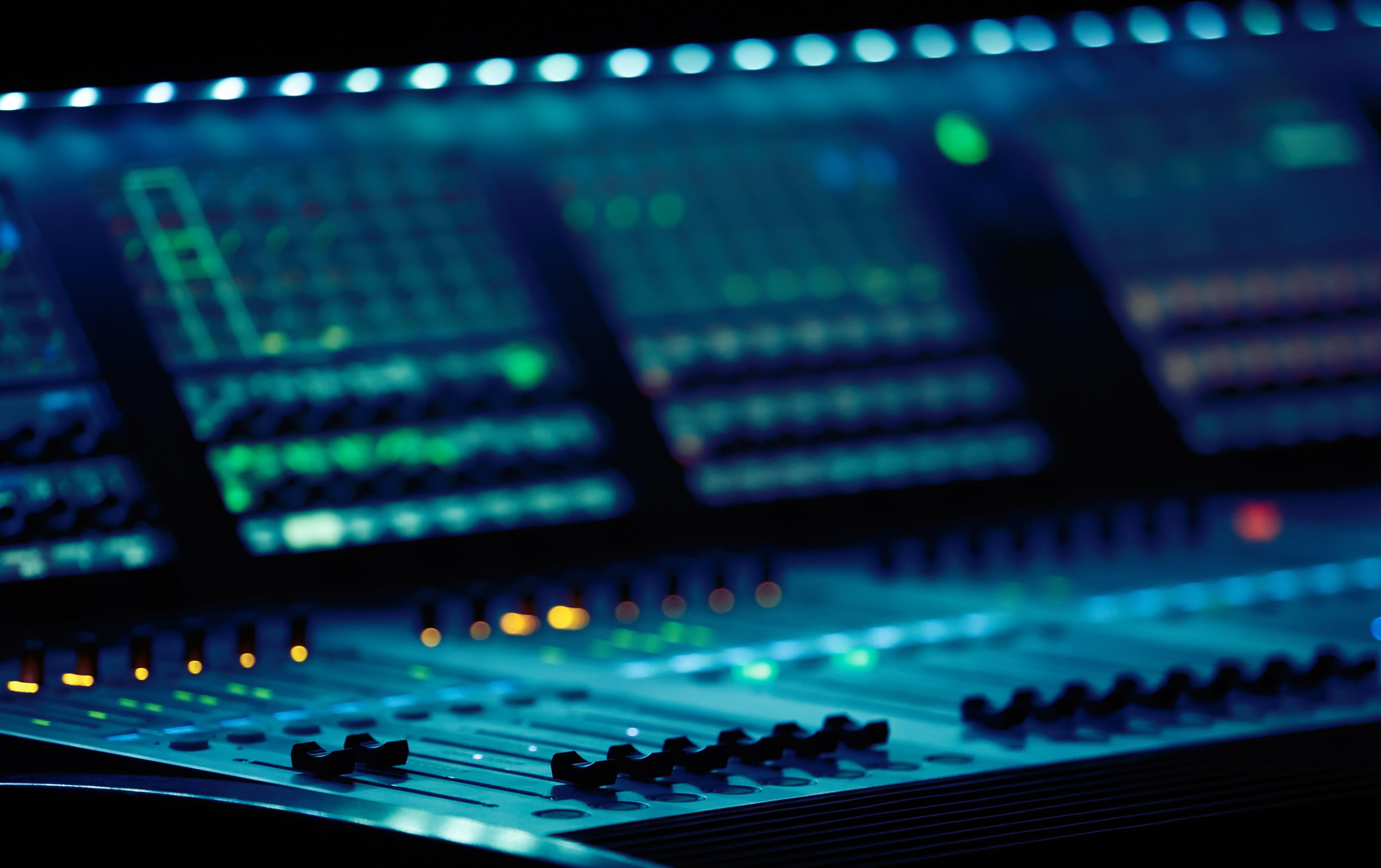 Close-up of a professional digital audio mixing console with glowing LED lights and faders. Perfect for music production, live sound, and studio recording.